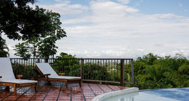 Zwei Liegestühle neben einem nassen Pooldeck überblicken eine üppige Landschaft unter einem bewölkten Himmel