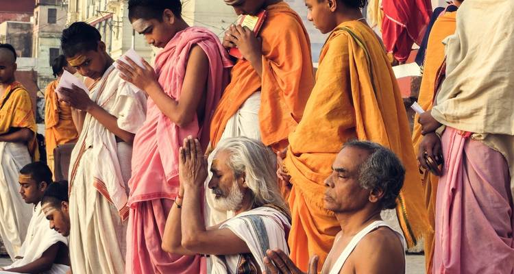 Men in traditional robes praying along a river bank.