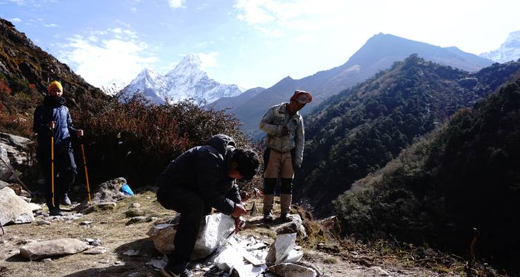 Three people in a mountainous landscape with snow-covered peaks in the background.