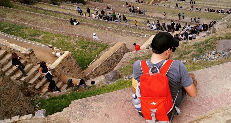 Un homme avec un sac à dos rouge assis sur un paysage en terrasses avec des gens en arrière-plan.