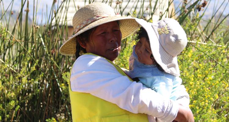 Une femme tenant un enfant dans la nature, toutes deux portant des chapeaux.