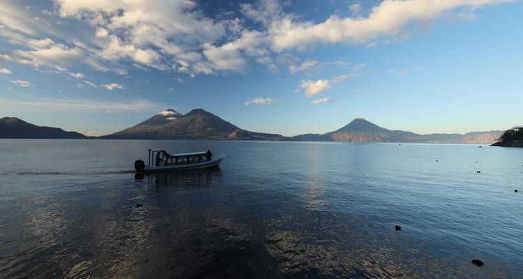 Een boot op een meer met vulkanen op de achtergrond.