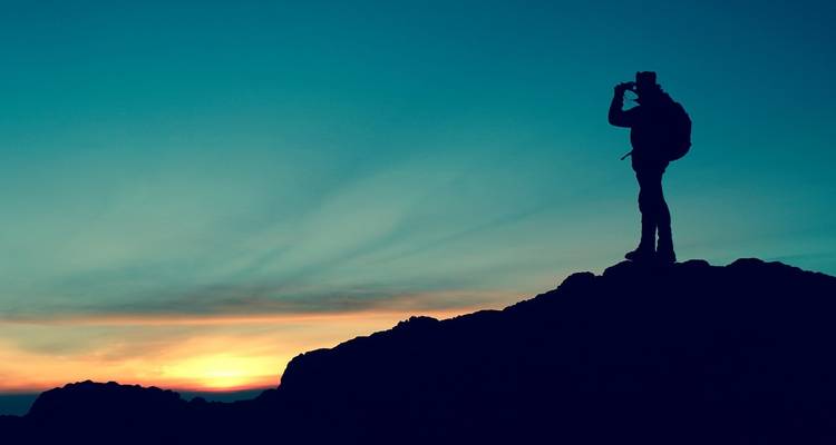 Silhouette eines Wanderers vor einem leuchtenden Sonnenuntergangshimmel.
