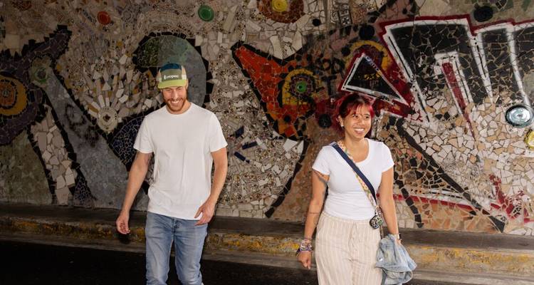 Deux personnes marchant devant un mur de mosaïque coloré.