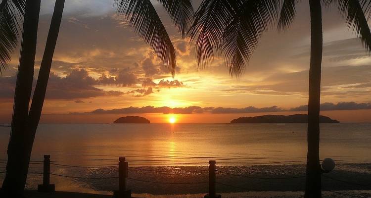 Prachtig zonsondergangzicht met palmbomen en eilanden in de verte.
