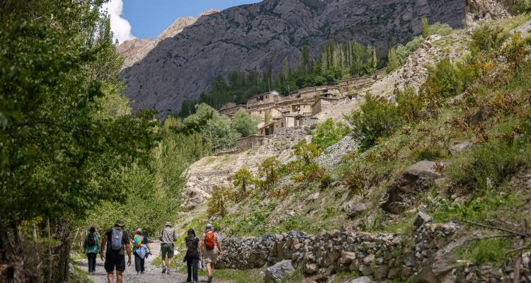 Los trekistas caminan por un sendero pedregoso hacia una aldea montañosa remota acurrucada en un valle verde de Asia Central.