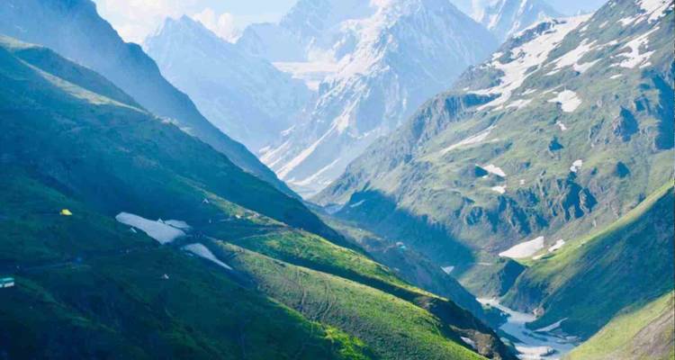 Des vallées vertes creusent à travers des crêtes himalayennes accidentées saupoudrées de neige sous un soleil éclatant.