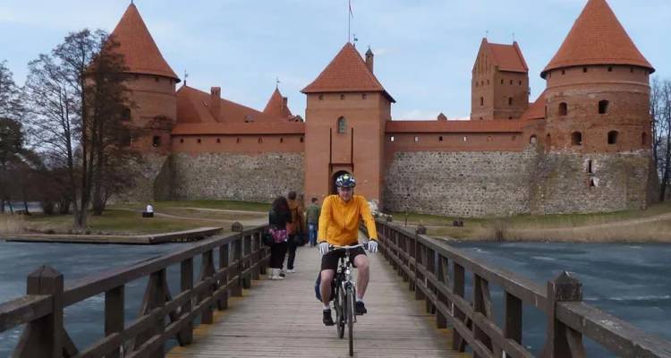 Wielrenner in geel shirt rijdt over houten brug naar het rode Trakai Eilandkasteel.