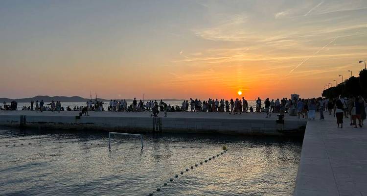 Crowd at a waterfront during sunset with a clear sky.