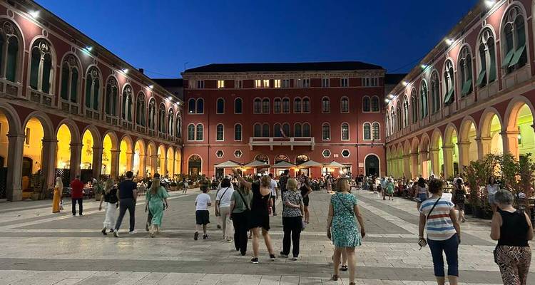 People walking in a brightly lit historical square at night.