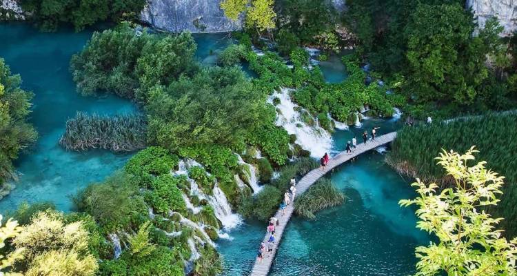 Luftaufnahme von Holzstegen, die türkisfarbene Becken und Wasserfälle im Nationalpark Plitvicer Seen überqueren.
