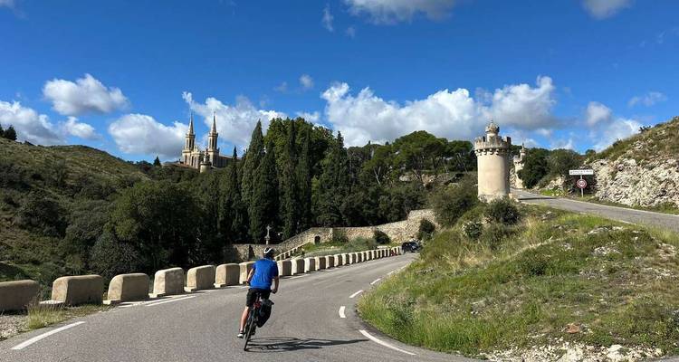 Fietser op een kronkelende weg omringd door heuvels en een historisch gebouw in de verte.