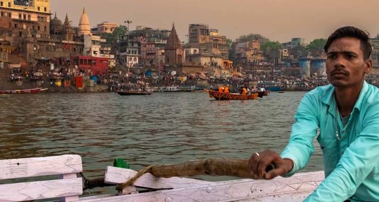 Le batelier rame le long du Gange avec les ghats colorés et les temples de Varanasi qui bordent le fleuve au crépuscule.
