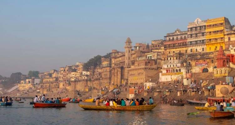 Drukke ghats van Varanasi bij zonsopgang met kleurrijke gebouwen en boten vol met pelgrims op de Ganges.
