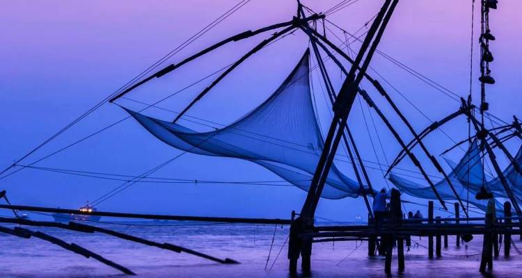 Les filets de pêche chinois se détachent en silhouette sur les eaux pourpre-bleu au crépuscule le long de la côte du Kerala.