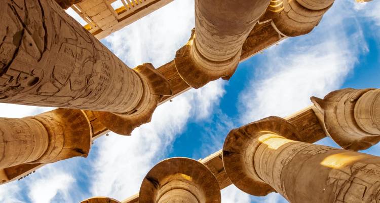 Dramatisch opwaarts uitzicht op kolossale uitgehouwen stenen zuilen in de Karnak Tempel tegen een blauwe lucht.
