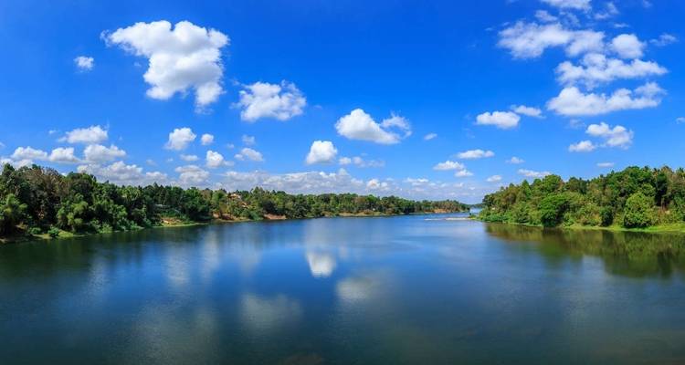 A tranquil lake surrounded by lush trees and a blue sky with clouds.
