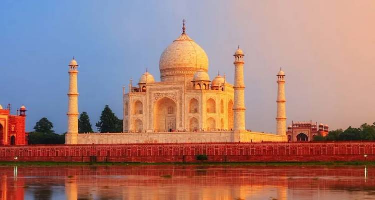 Het ongerepte witte marmer van de Taj Mahal weerspiegelt warme zonsondergangtinten, gespiegeld in het stilstaande water van de Yamuna-rivier eronder.