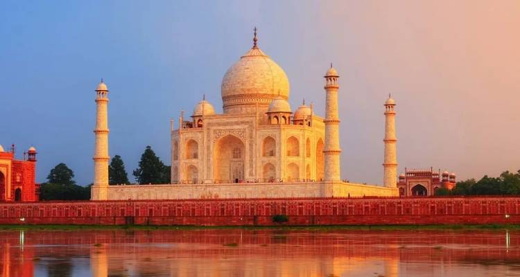 El Taj Mahal brilla con luz pastel reflejada en el río tranquilo al atardecer.