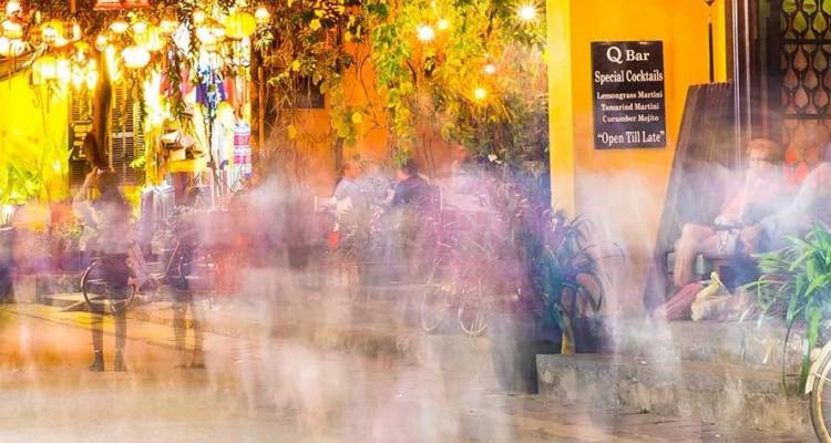 Scène nocturne d'une rue de Hoi An avec des foules en mouvement flou et des lanternes illuminées.