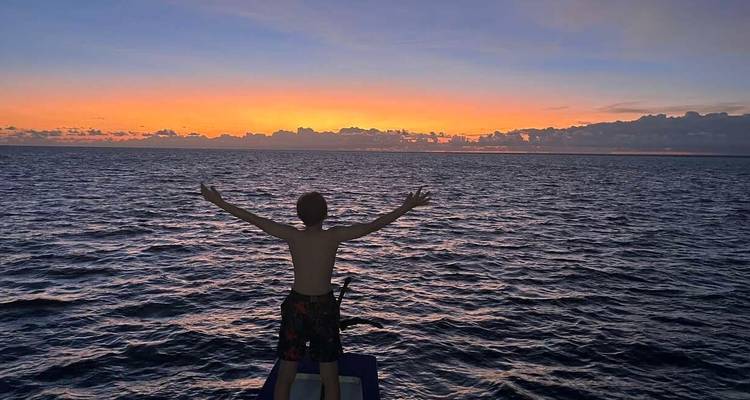 Personne debout sur un bateau les bras étendus au coucher du soleil.