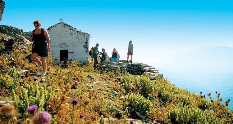 Los excursionistas se congregan cerca de una pequeña capilla encalada en la cima de una cresta cubierta de flores con amplias vistas a las montañas