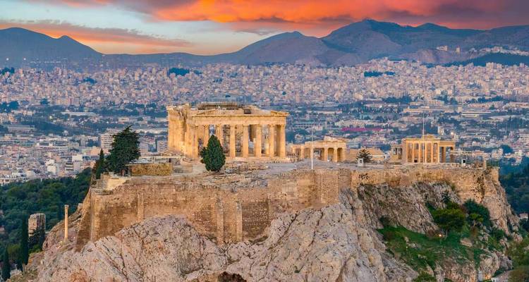 Vue panoramique de l'Acropole et du Parthénon au sommet d'une colline rocheuse avec des teintes pastel de coucher de soleil et des montagnes au-delà d'Athènes.