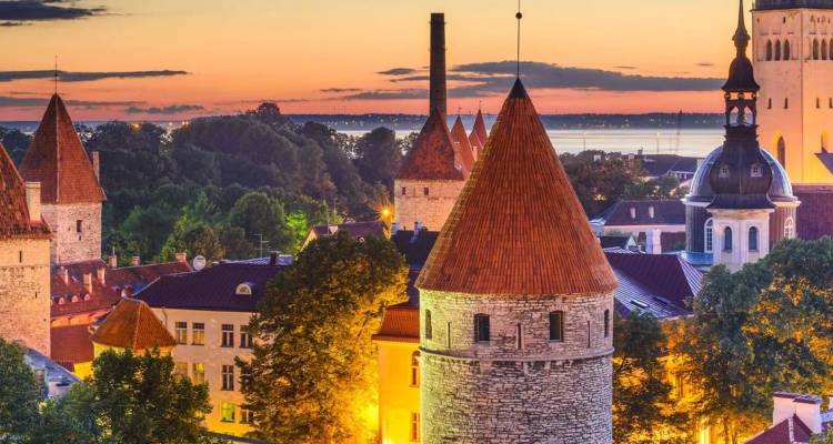 Farbenfroher Sonnenuntergang über mittelalterlichen Steintürmen und rotgedeckten Dächern einer alten europäischen Stadt am Meer.
