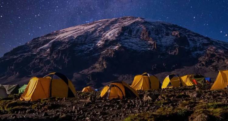 Rijen gele tenten onder de sterrenhemel en de sneeuwbedekte top van de Kilimanjaro 's nachts