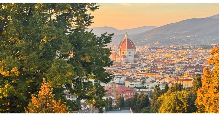 Vue panoramique de Florence avec le dôme du Duomo s'élevant au-dessus de la ville au coucher du soleil doré, encadrée par les arbres d'automne.
