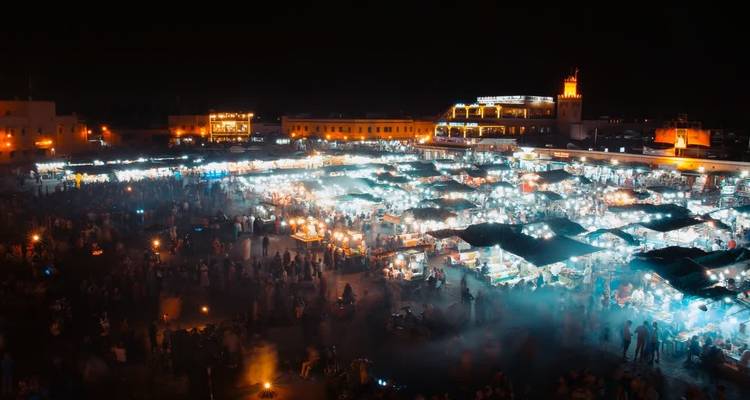 Escena nocturna de mercado con humo elevándose y puestos iluminados.