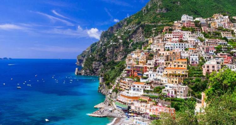 Village coloré de Positano en bordure de falaise s'écoulant vers la mer Tyrrhénienne d'un bleu profond parsemée de bateaux sous un ciel dégagé.