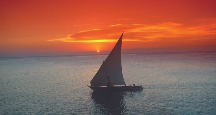 Velero silueteado contra una impresionante puesta de sol naranja.