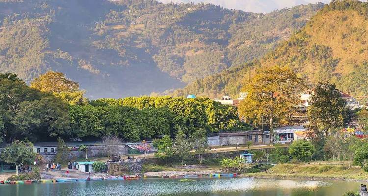 Üppig grüne Hügel rahmen einen friedlichen See unterhalb der nebligen Ausläufer des Himalaya in der Nähe von Pokhara ein.