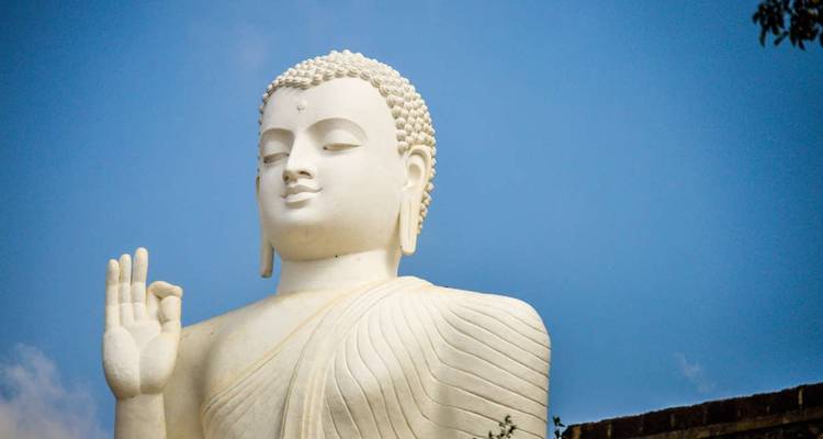 Gros plan de la même statue de Bouddha blanche et sereine se détachant sur un ciel bleu.