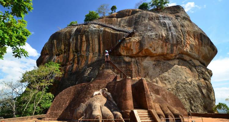 Les visiteurs montent les escaliers raides du rocher de Sigiriya encadrés par un ciel bleu et de la verdure.