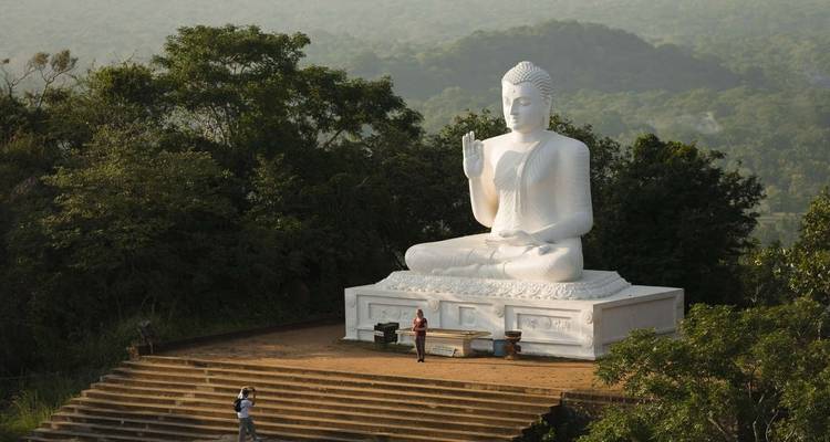 Large white Buddha statue on a hill with people nearby.