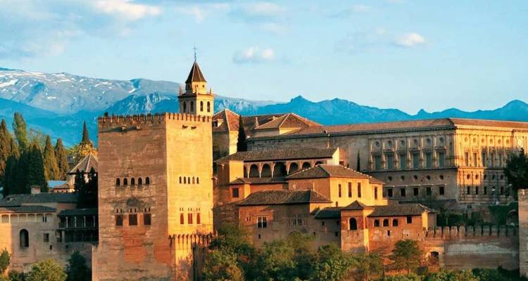 Le complexe palatial de l'Alhambra baigné de lumière chaude avec les montagnes de la Sierra Nevada en arrière-plan.