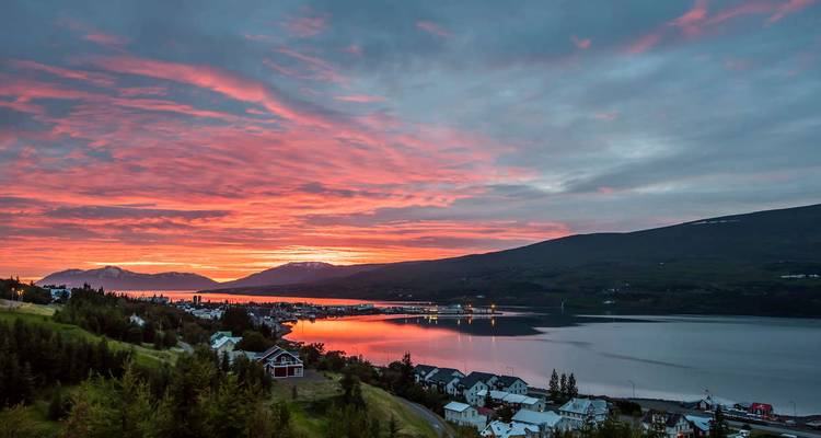 Coucher de soleil aux teintes rouges et orangées éclatantes au-dessus du fjord d'Akureyri, se reflétant dans l'eau calme avec les lumières de la ville en dessous.