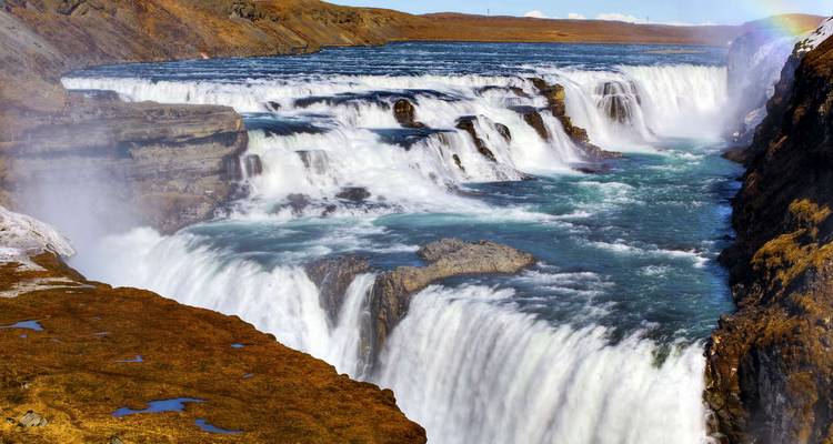 La cascade majestueuse et multi-étages de Gullfoss se précipite dans un canyon au milieu de la brume et de la lumière du soleil.