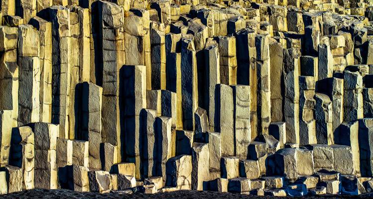 Gros plan des colonnes de basalte dramatiques et verticales le long de la côte sud de l'Islande, éclairées par un soleil bas.