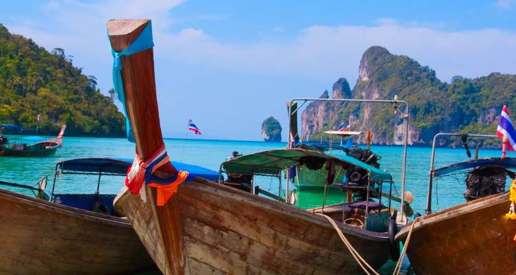 Barcos de madera con cola larga tradicionales amarrados en agua turquesa con islas de piedra caliza dramáticas de fondo