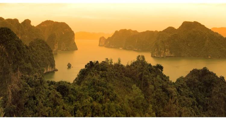 La brume dorée du coucher de soleil enveloppe les îles calcaires en forme de pain de sucre et les eaux émeraude de la baie d'Ha Long.