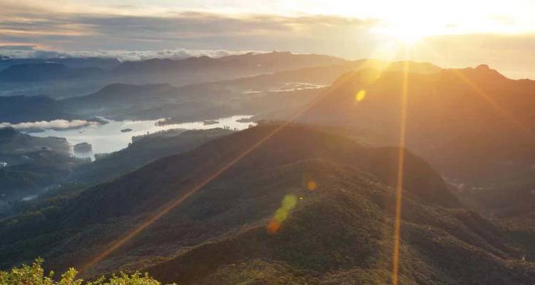 Zonsopkomststralen vallen over mistige bergketens en een kronkelend meer in centraal Sri Lanka.