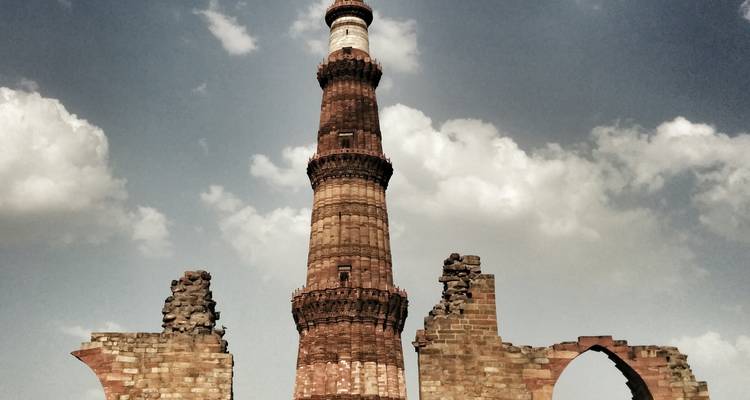 Minarete histórico con ruinas rodeado de cielos nublados.