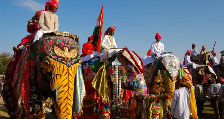 Elefantes decorados de colores con jinetes vestidos con atuendos tradicionales.