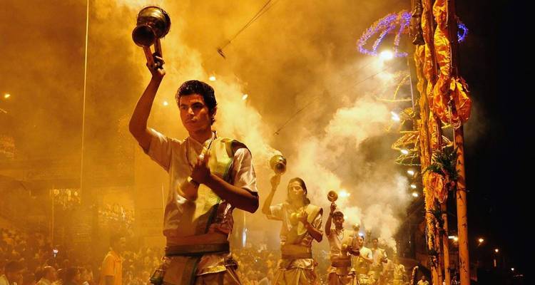 Los sacerdotes realizan la ceremonia ardiente del Ganga Aarti en los escalones abarrotados de los ghats de Varanasi, con el humo naranja y las llamas iluminando la noche.
