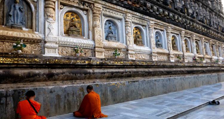 Dos monjes con túnicas azafrán se sientan en contemplación junto a la pared exterior intrincadamente tallada del Templo Mahabodhi.