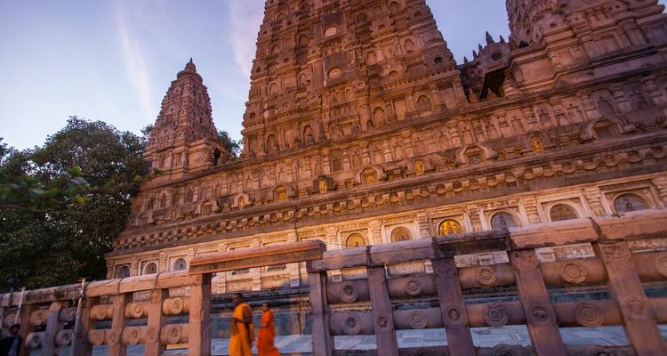 Los colores del crepúsculo tiñen la imponente aguja del Templo Mahabodhi mientras dos monjes caminan junto a las barandillas de piedra.