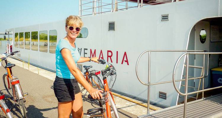 Una mujer con una bicicleta cerca de un barco llamado "MARIA".